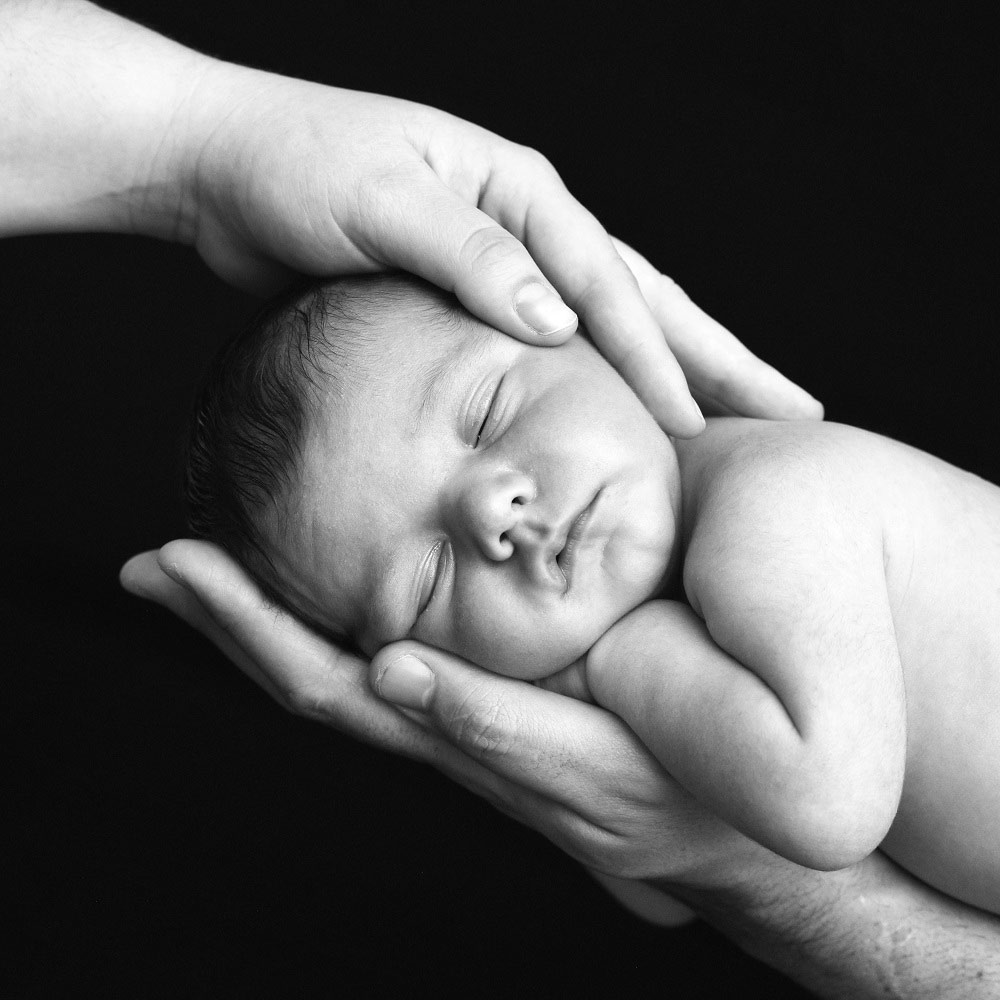 photographie noir et blanc d'un bébé quelques jours après la naissance avec la main du papa etla main de la maman, par la photographe Marie Salis à Toulon